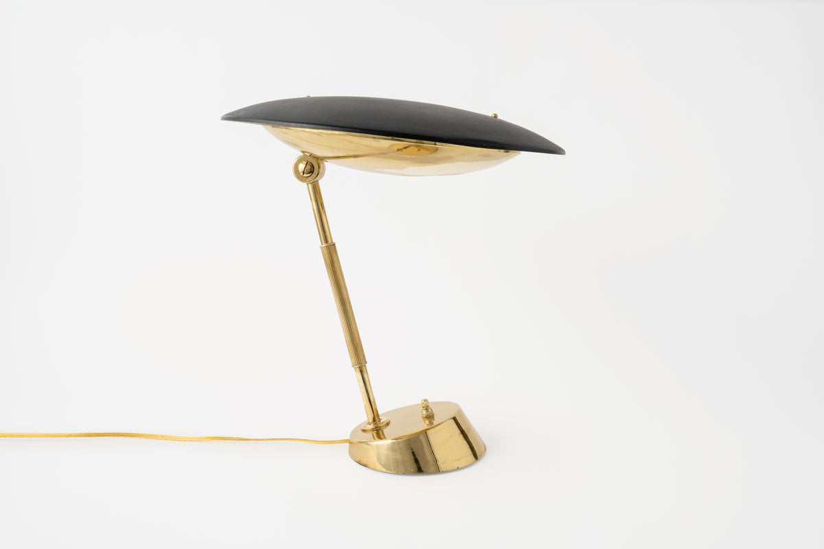 A vintage table lamp with a black shade and a brass base and pole, isolated on a white background.