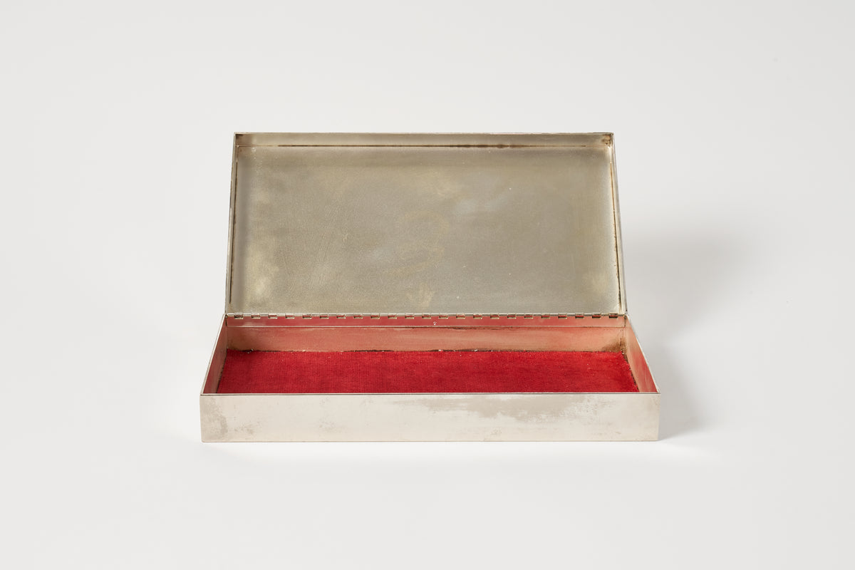 A silver case with its lid propped open, revealing a bright red velvet-lined interior, set against a plain light gray background.