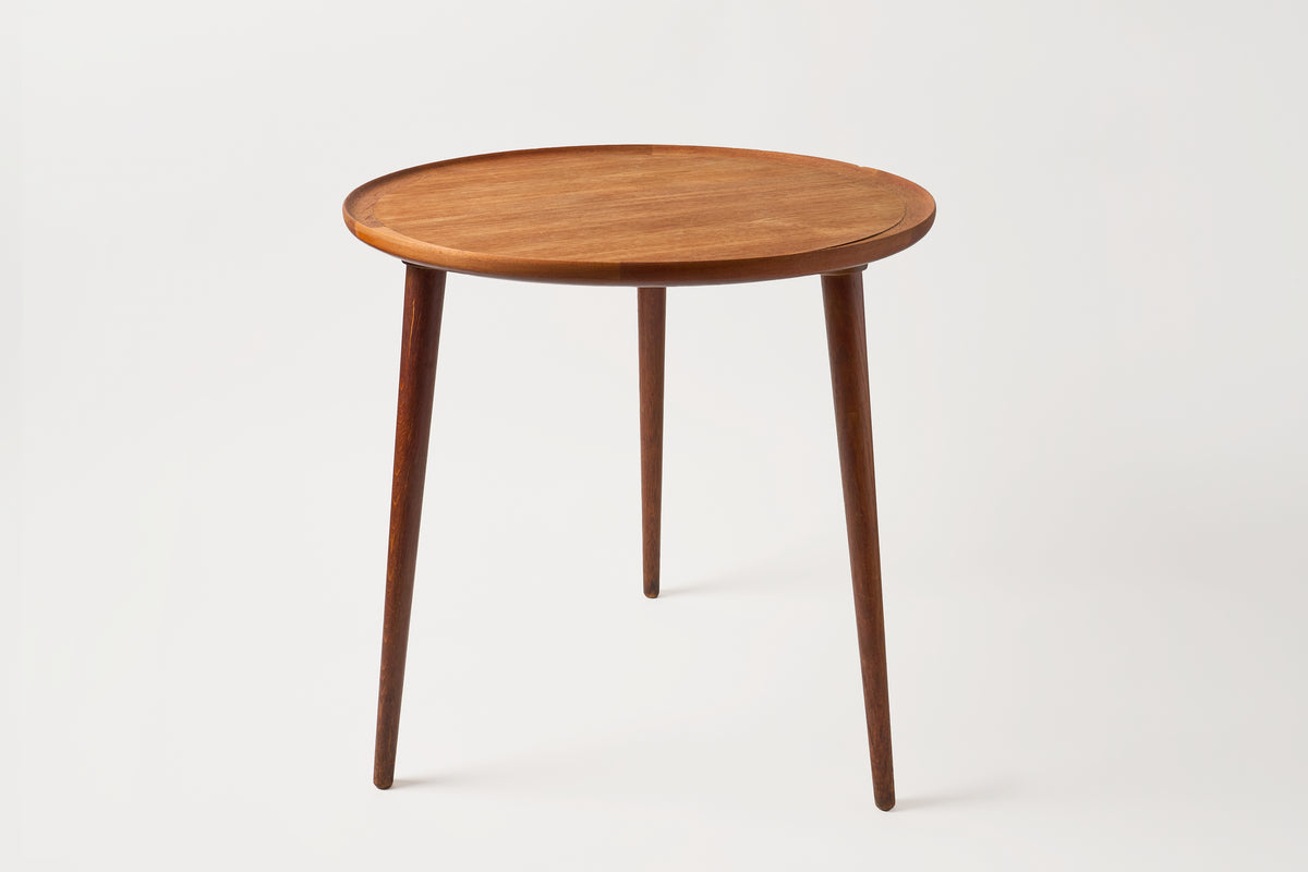 A round wooden side table with a warm medium-brown finish and four tapered legs, photographed against a clean light gray studio background.