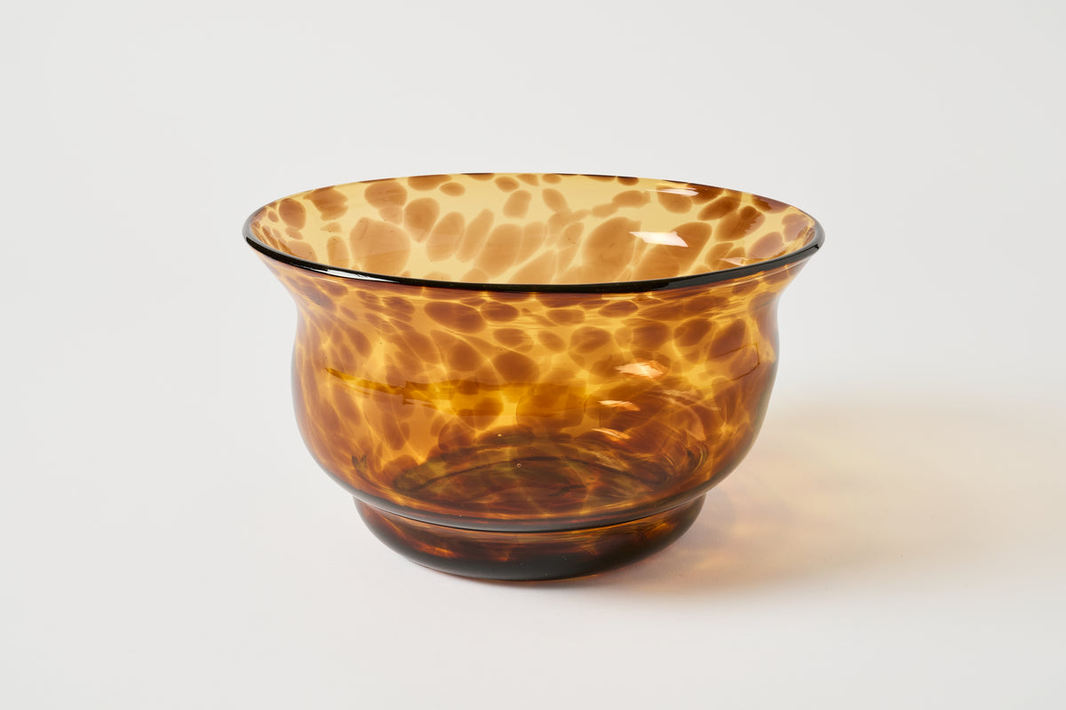 An amber brown translucent glass bowl with a mottled, marbled pattern resembling tortoiseshell, set against a plain light gray background.