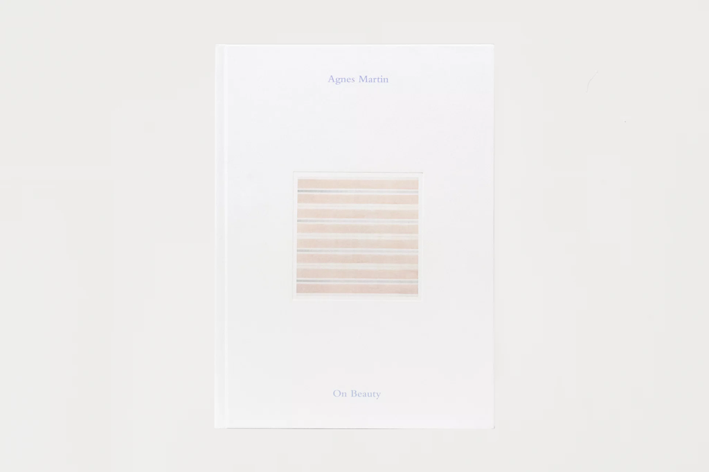 A white book or booklet titled 'Agness Martin On Beauty' with a small central striped square illustration, photographed against a light gray background.