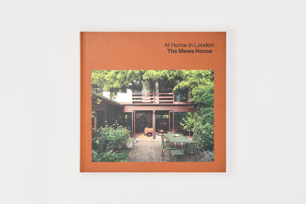 A hardcover book titled 'At Home in London: The Mews House' with a terracotta orange-brown cover and a central photograph of a house surrounded by greenery, shown against a light gray background.