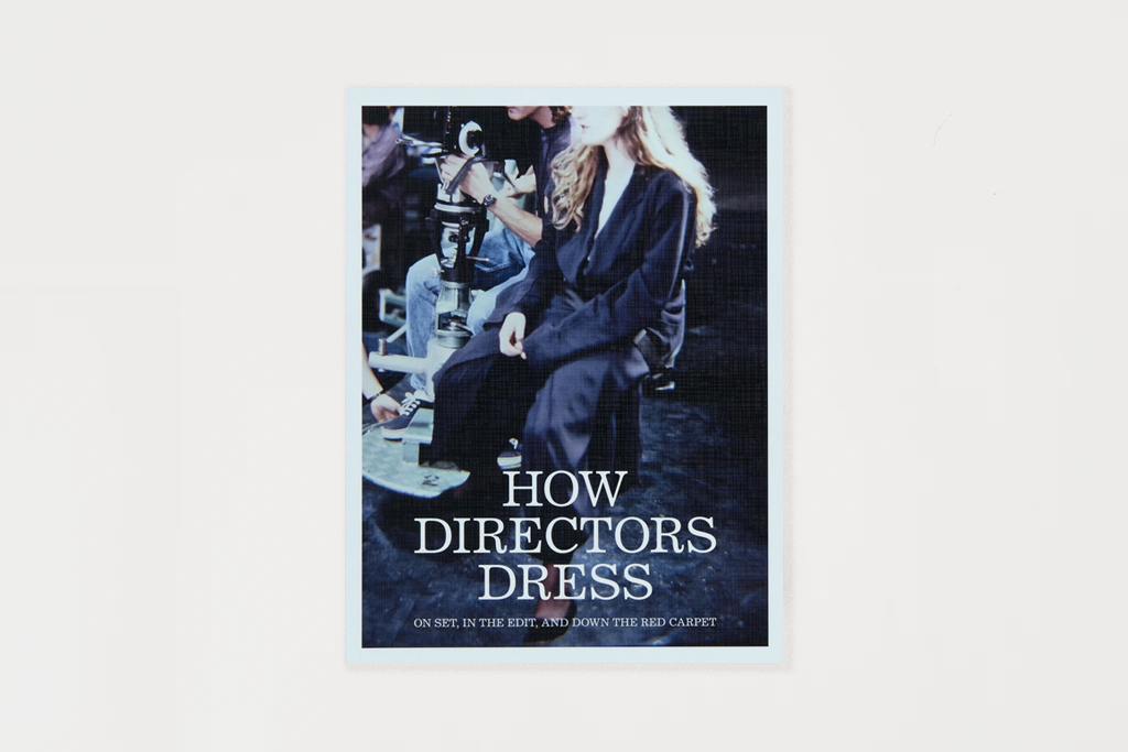 A book cover titled 'HOW DIRECTORS DRESS' shown centered on a light gray background. The cover features a dark photo of a woman in a black dress on a film set, with white title text overlaid near the bottom.