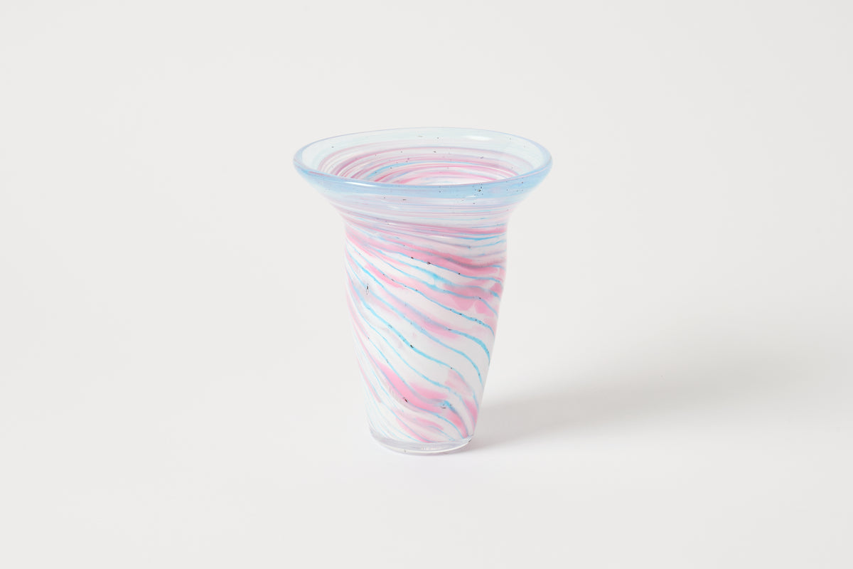 A small flared glass cup with a swirled pattern of pink, blue, and white glass, set against a plain light gray background.