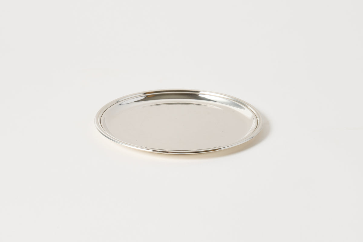 A small round silver plate with a polished metallic finish, photographed from a top-down perspective on a clean white background.
