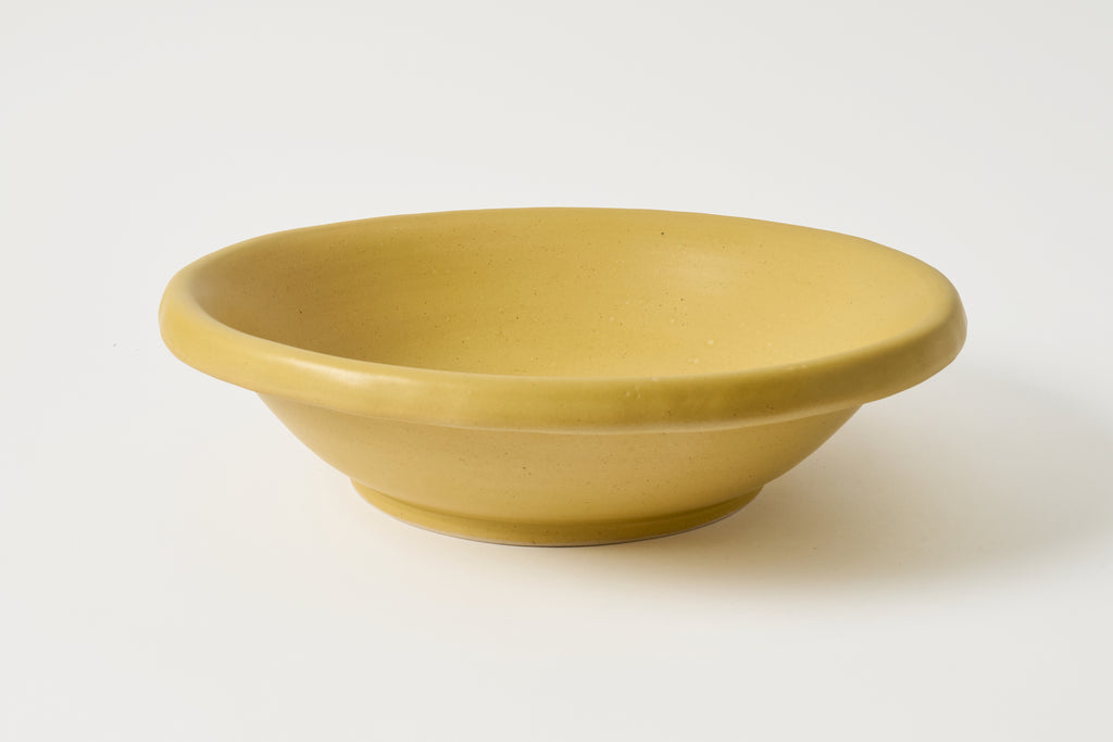 A large, wide-mouthed ceramic bowl in a matte mustard yellow color, photographed on a clean white background.