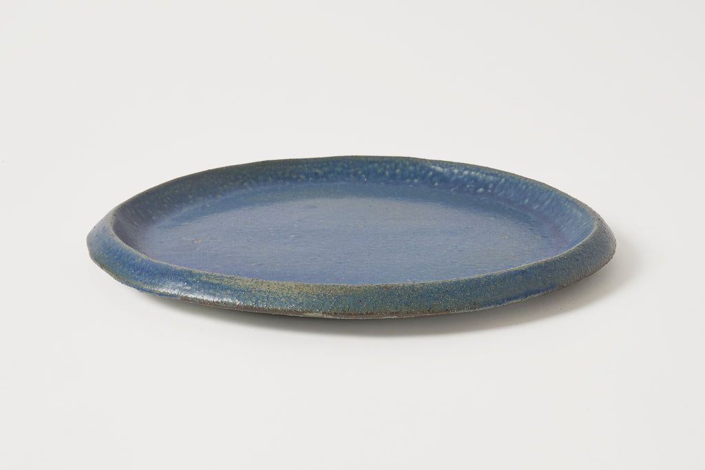 A round ceramic plate with a textured, speckled blue glaze and a slightly darker rim, photographed on a clean white background.