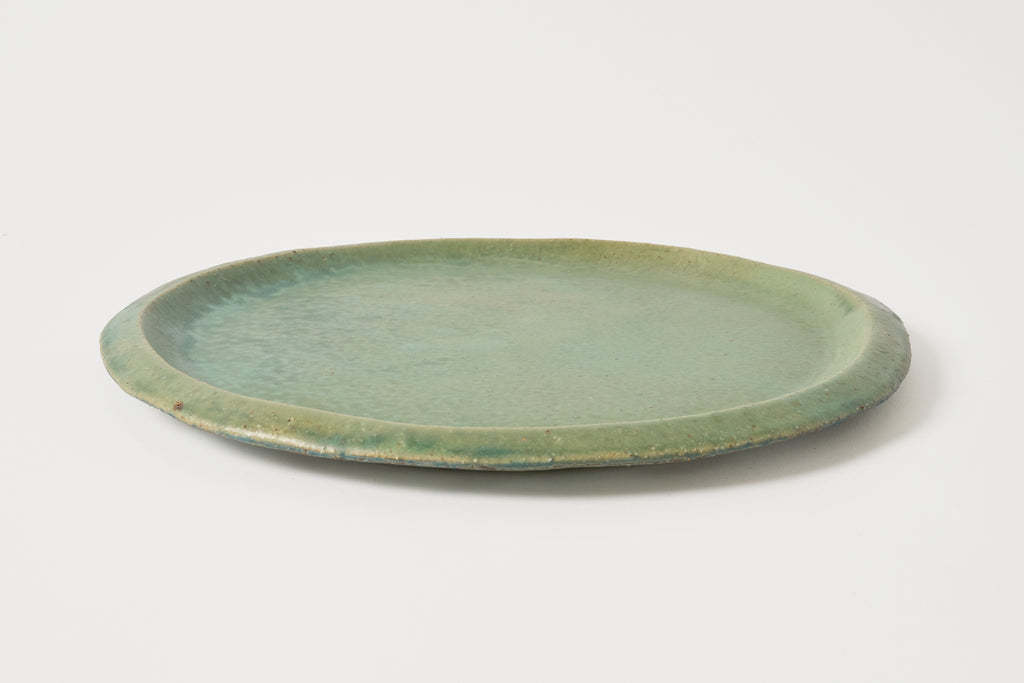 A round ceramic plate with a light green glaze, photographed from a side angle on a clean white background.