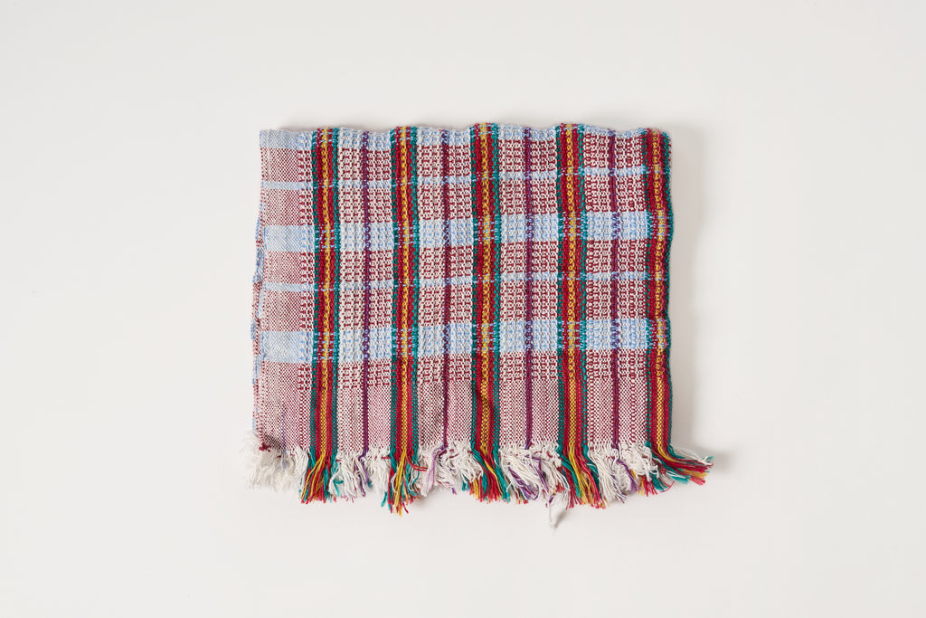 A square woven towel with a multicolor plaid pattern in shades of red, blue, green, and purple, finished with fringed edges, shown against a plain white background.