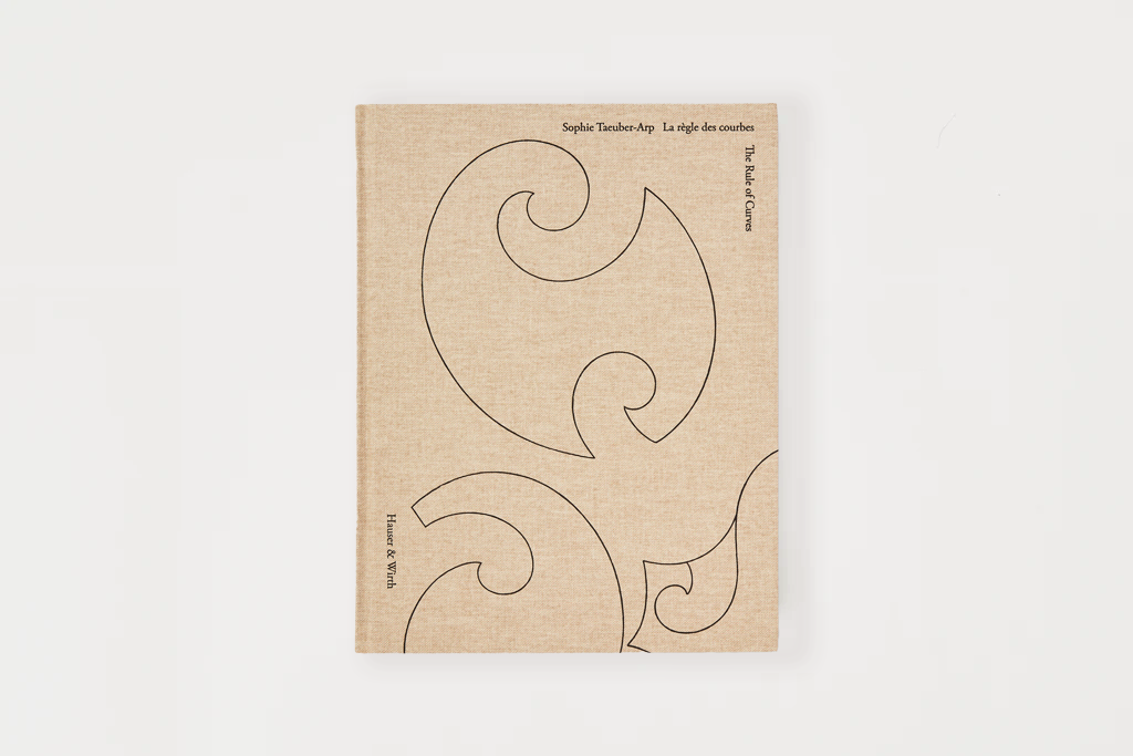 A square fabric-covered book or journal with a light beige linen cover, featuring black line-art scroll designs and small printed text near the top and along the left edge, photographed against a clean white background.